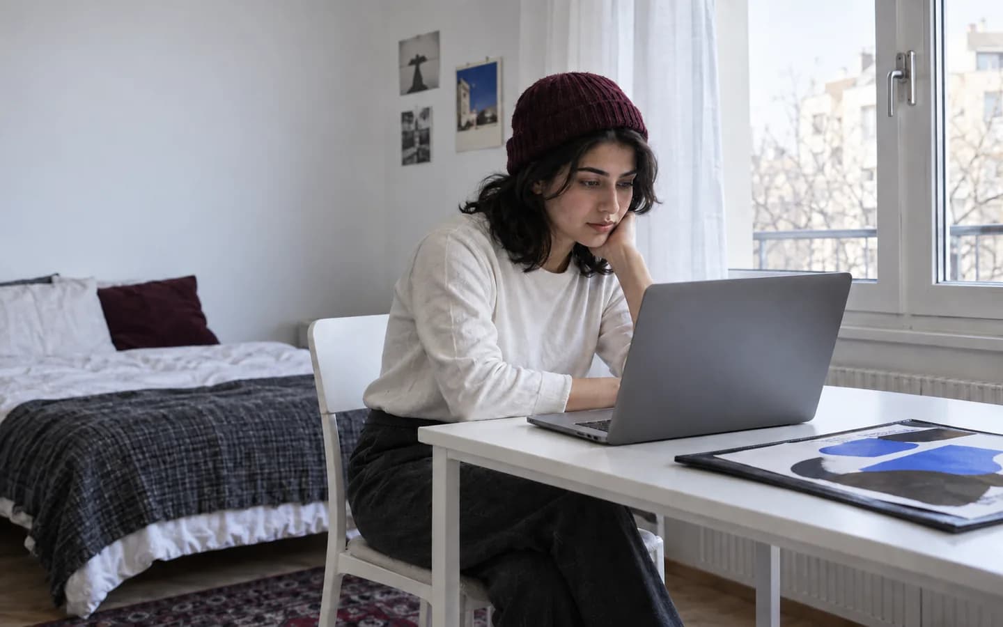هنرجو با کلاه بافتنی در حال مطالعه با لپ‌تاپ، کنار نمونه پروژه طراحی